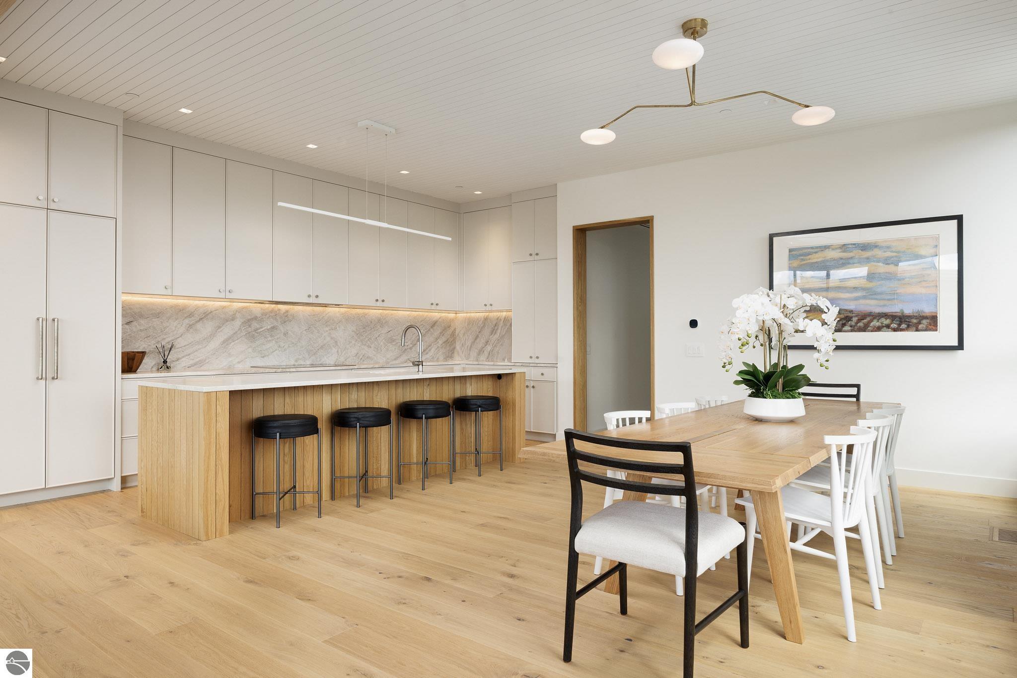 Kitchen and dining area with a wood-front island, black stools, and a long dining table.
