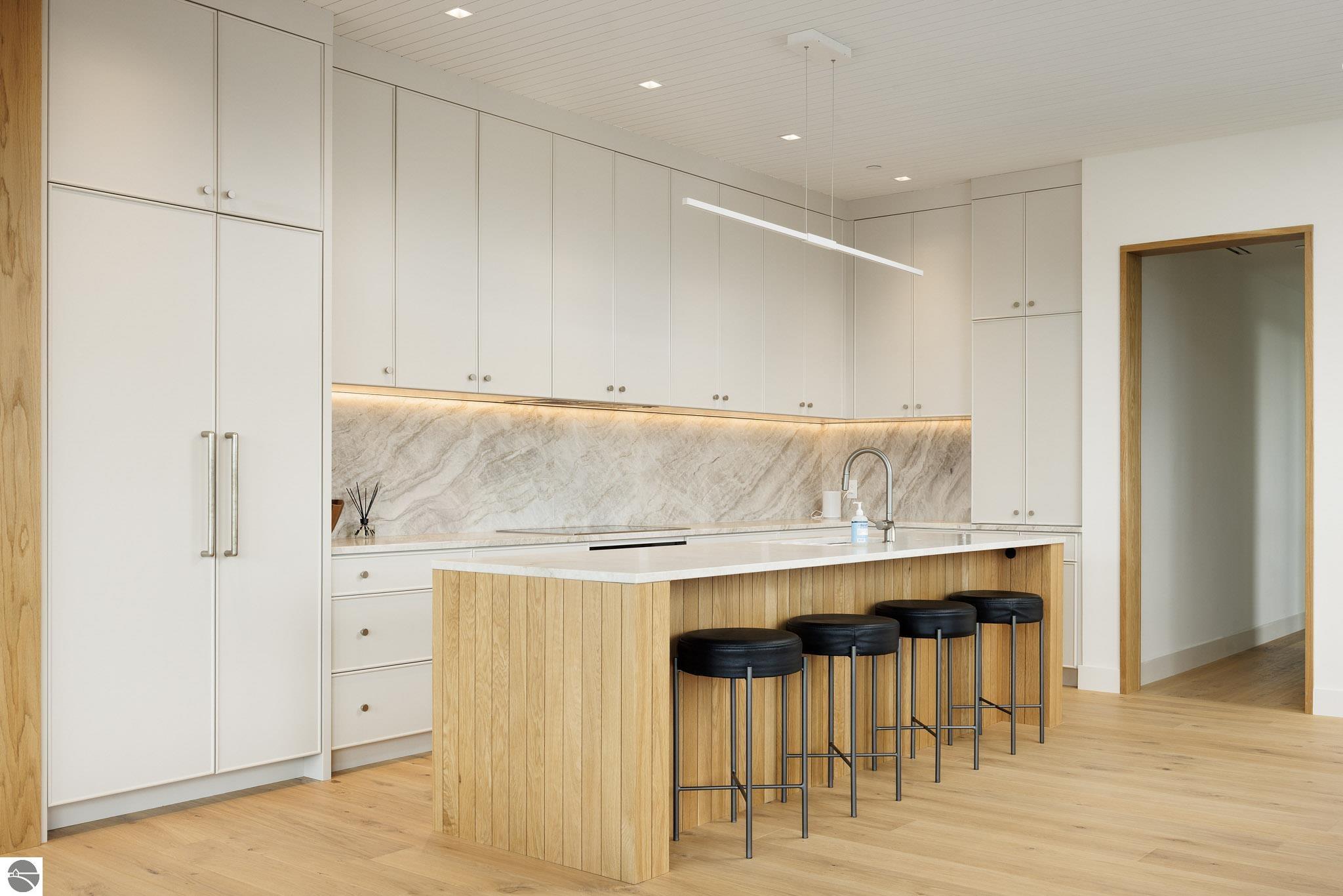 Modern kitchen with white cabinetry, a veined stone backsplash, and a wood-paneled island with four stools.