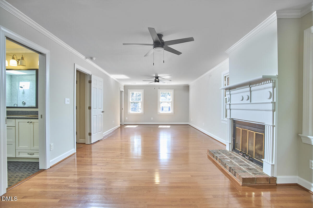 Empty living room with hardwood floors, a white fireplace, ceiling fans, and two rear windows.