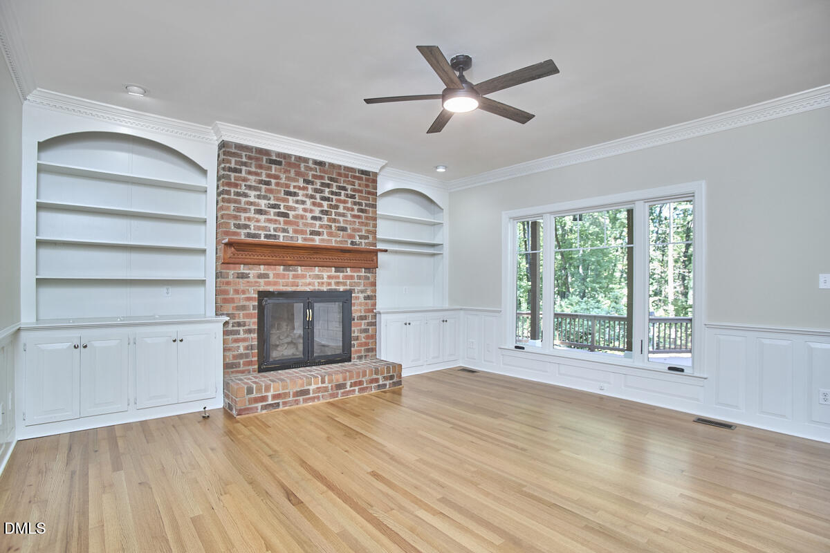 Living room with a brick fireplace, built-in shelves, hardwood floors, and large windows.