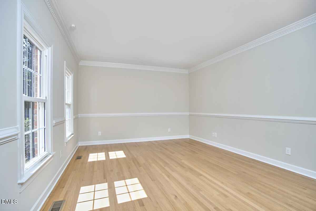 Empty room with hardwood floors, decorative molding, and two tall windows.