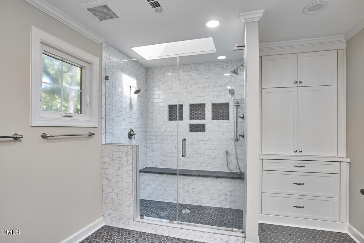 Bathroom with a glass-enclosed marble-look shower, dark mosaic floor, and built-in white cabinetry.