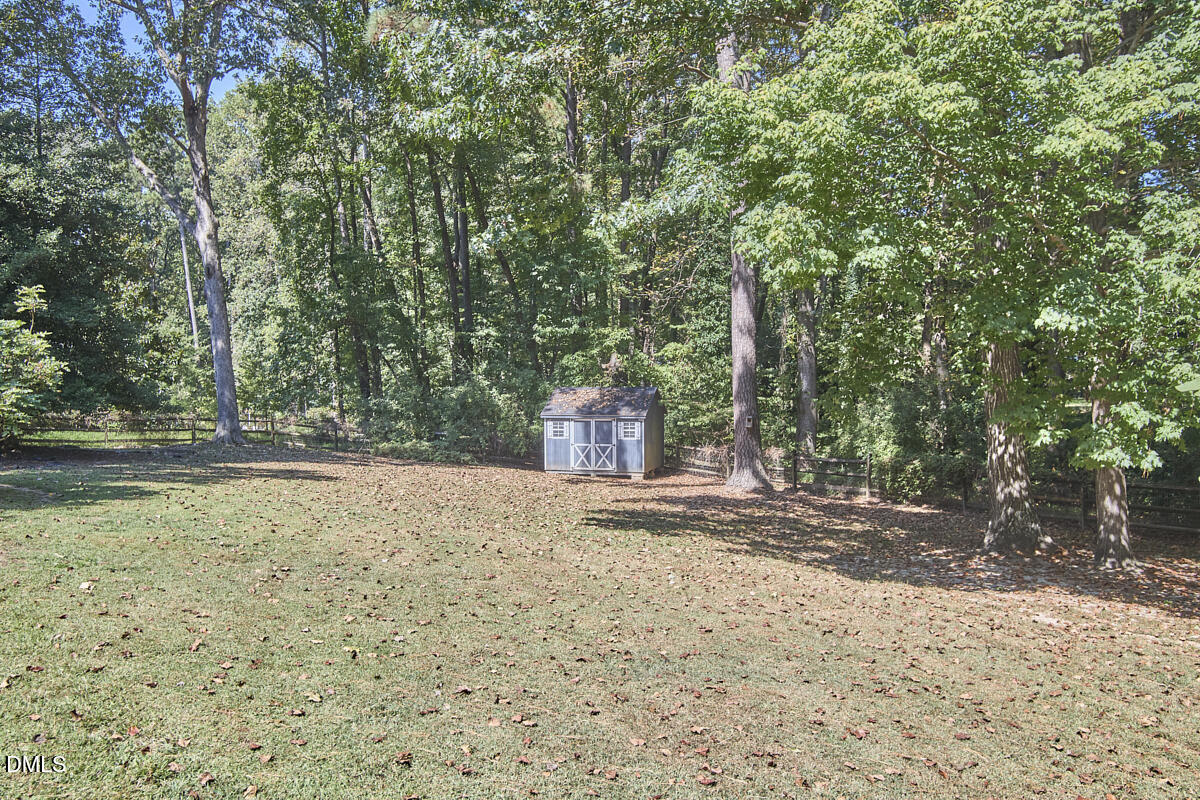 Wooded backyard with a broad lawn, split-rail fence, and small storage shed.