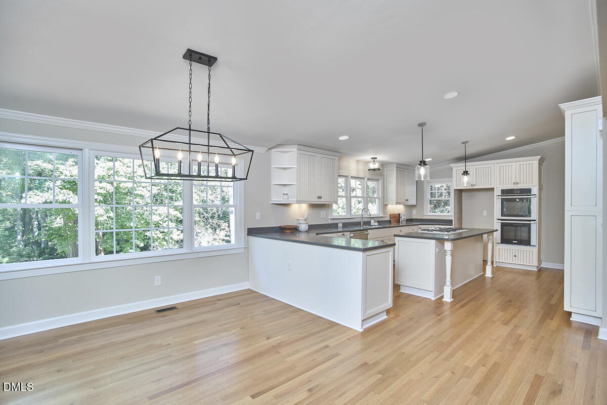 Open-plan kitchen with white cabinetry, dark countertops, a central island, and large tree-facing windows.
