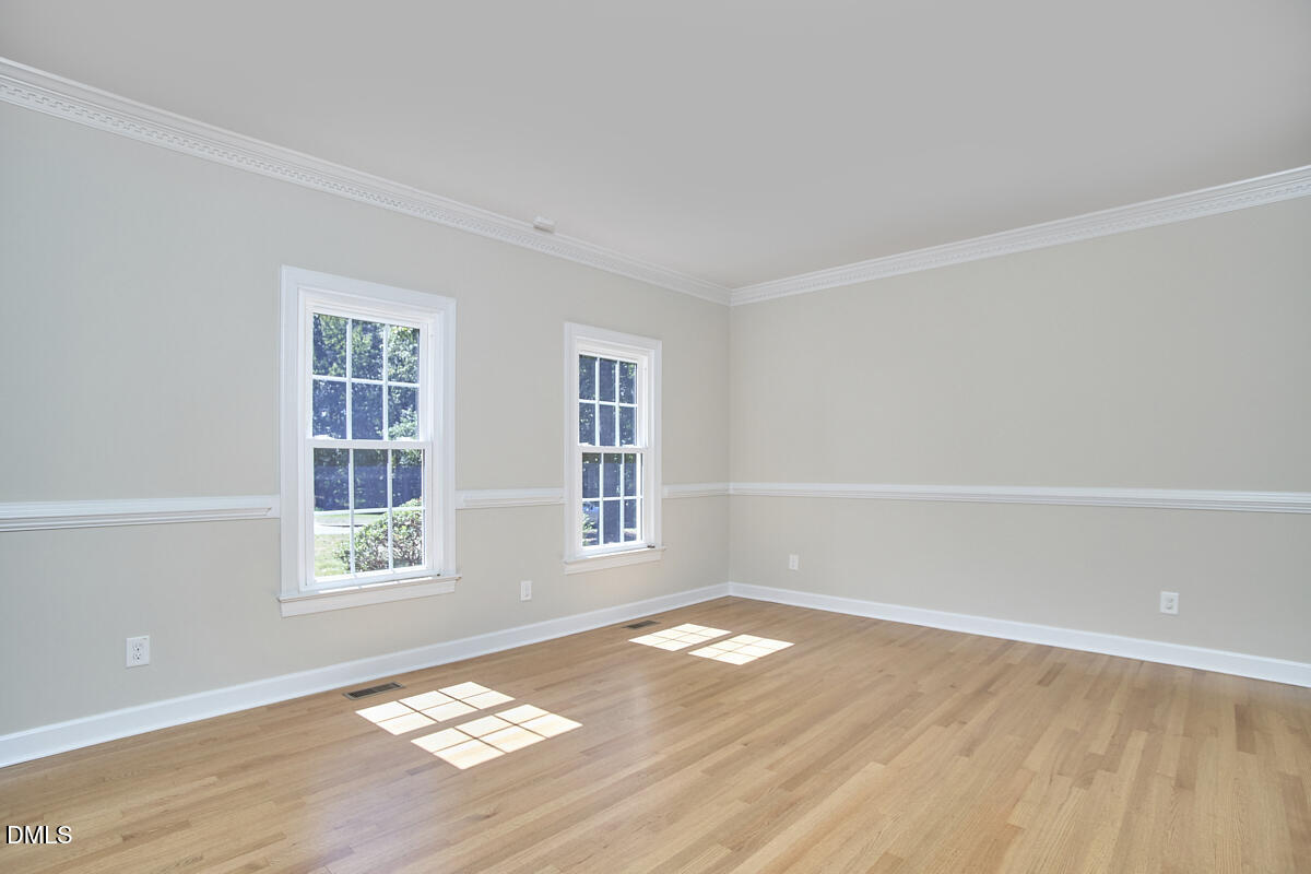 Empty room with hardwood floors, two windows, crown molding, and chair-rail trim.