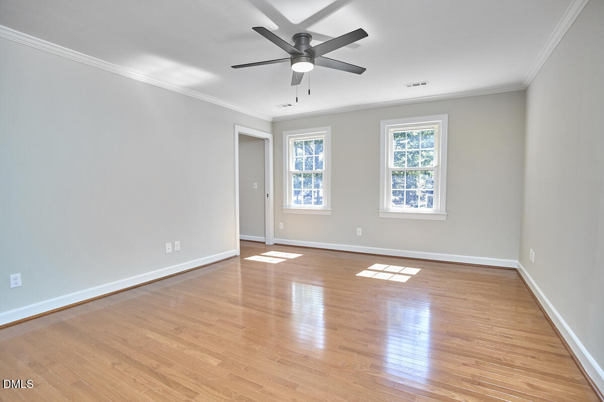 Empty room with hardwood floors, two windows, and a modern ceiling fan.