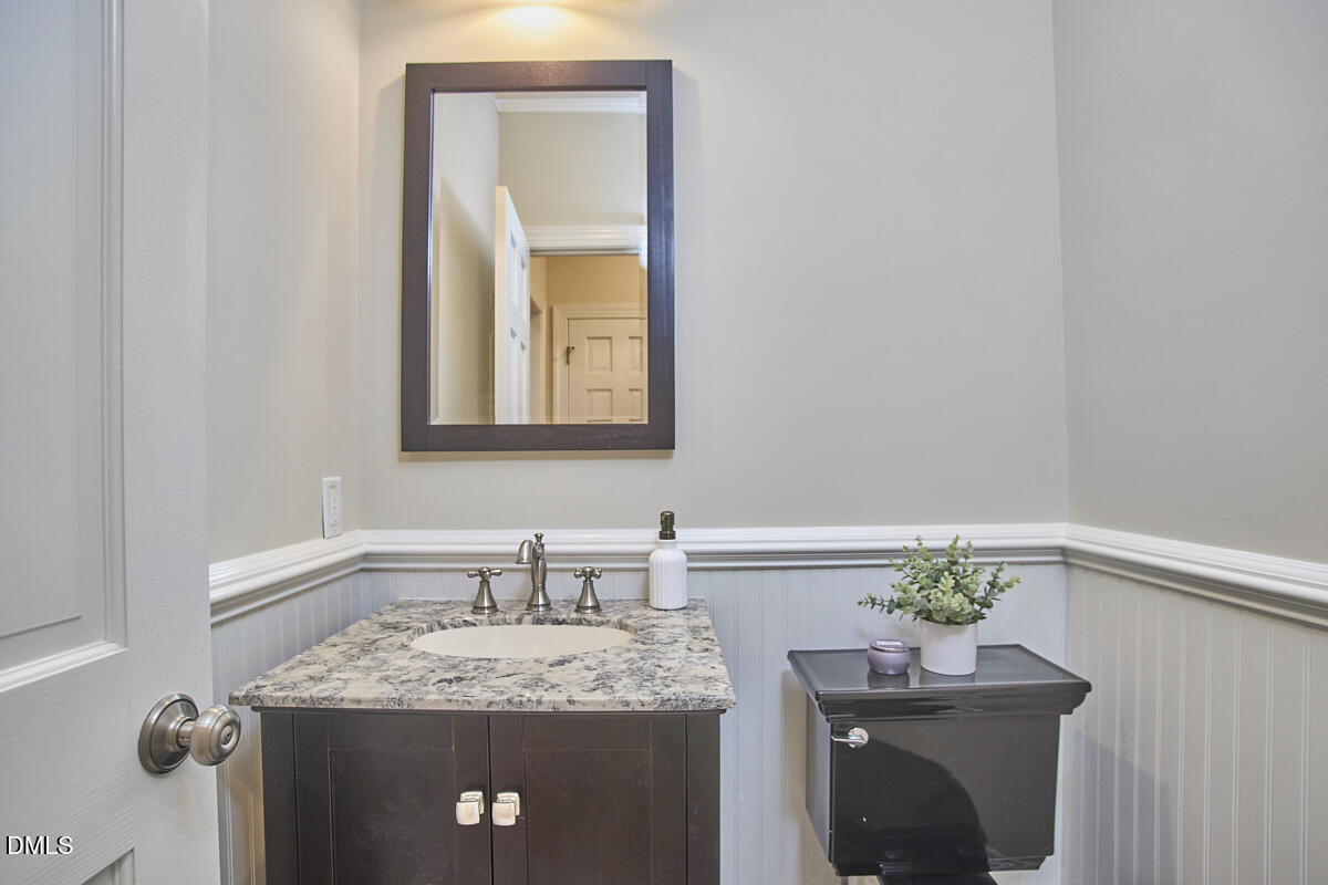 Bathroom with a dark stone-topped vanity, oval sink, white wainscoting, and dark toilet.