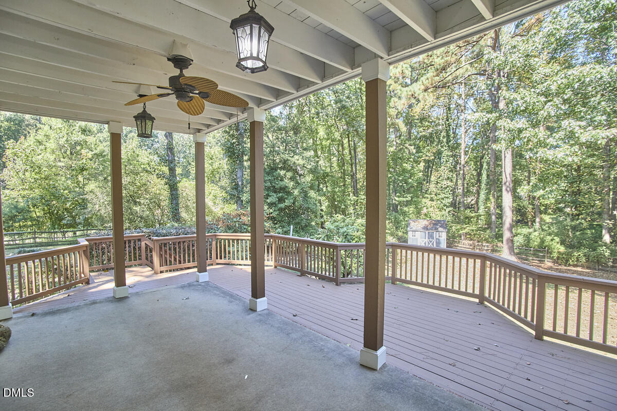 Covered patio and wooden deck overlooking a wooded backyard, with a ceiling fan and hanging lights.