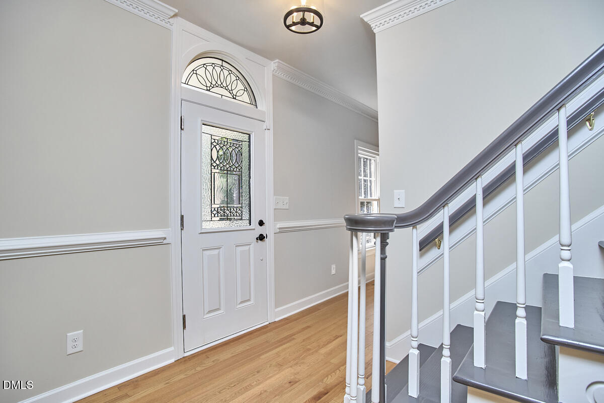 Entry foyer with decorative glass front door, hardwood floors, and staircase with dark handrails.