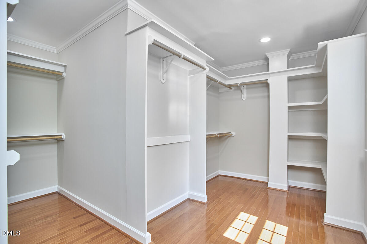 Empty walk-in closet with built-in hanging rods and shelves above polished hardwood floors.