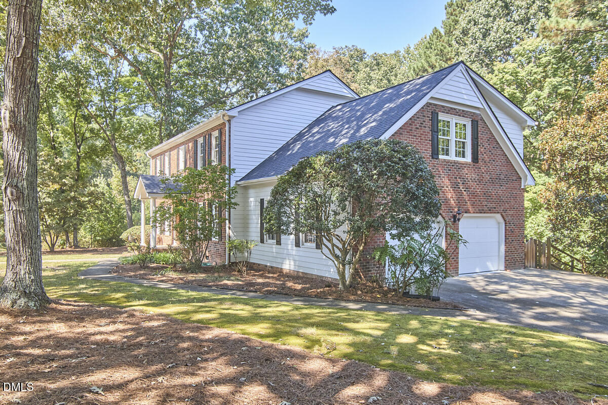 Two-story brick and white-sided home with an attached garage, mature trees, and a landscaped lawn.