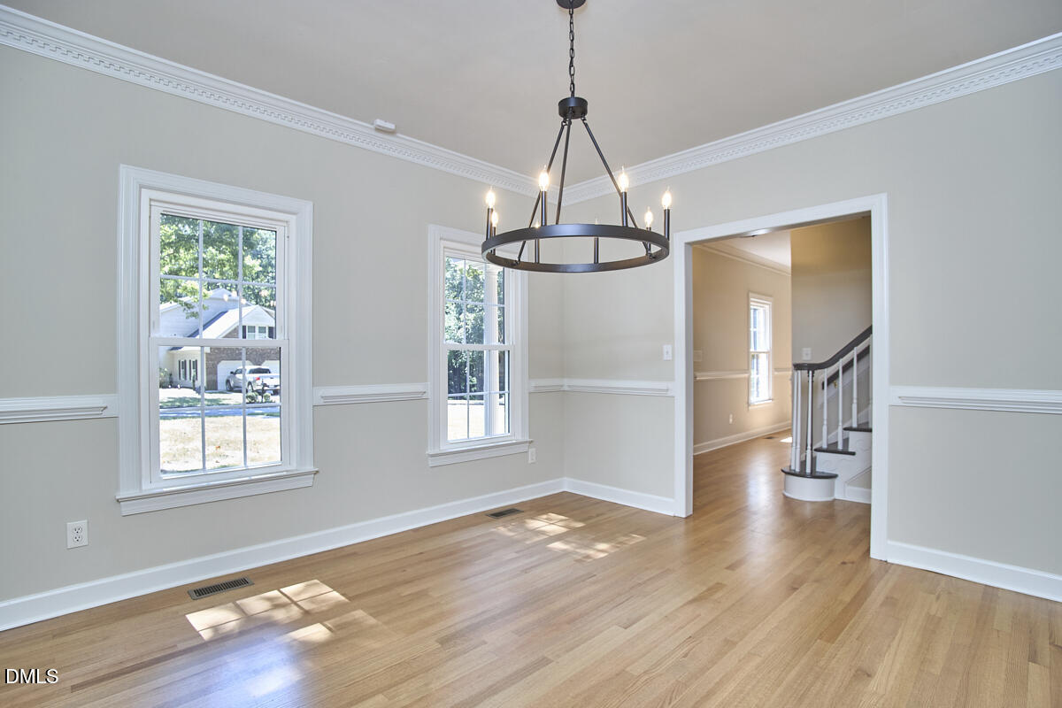 Empty dining room with hardwood floors, a circular chandelier, and a doorway to the staircase.