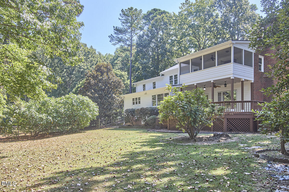 House with a raised deck and screened porch overlooking a leafy, tree-lined backyard.