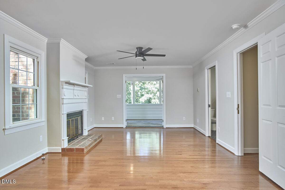 Vacant living room with hardwood floors, white fireplace, and ceiling fan.