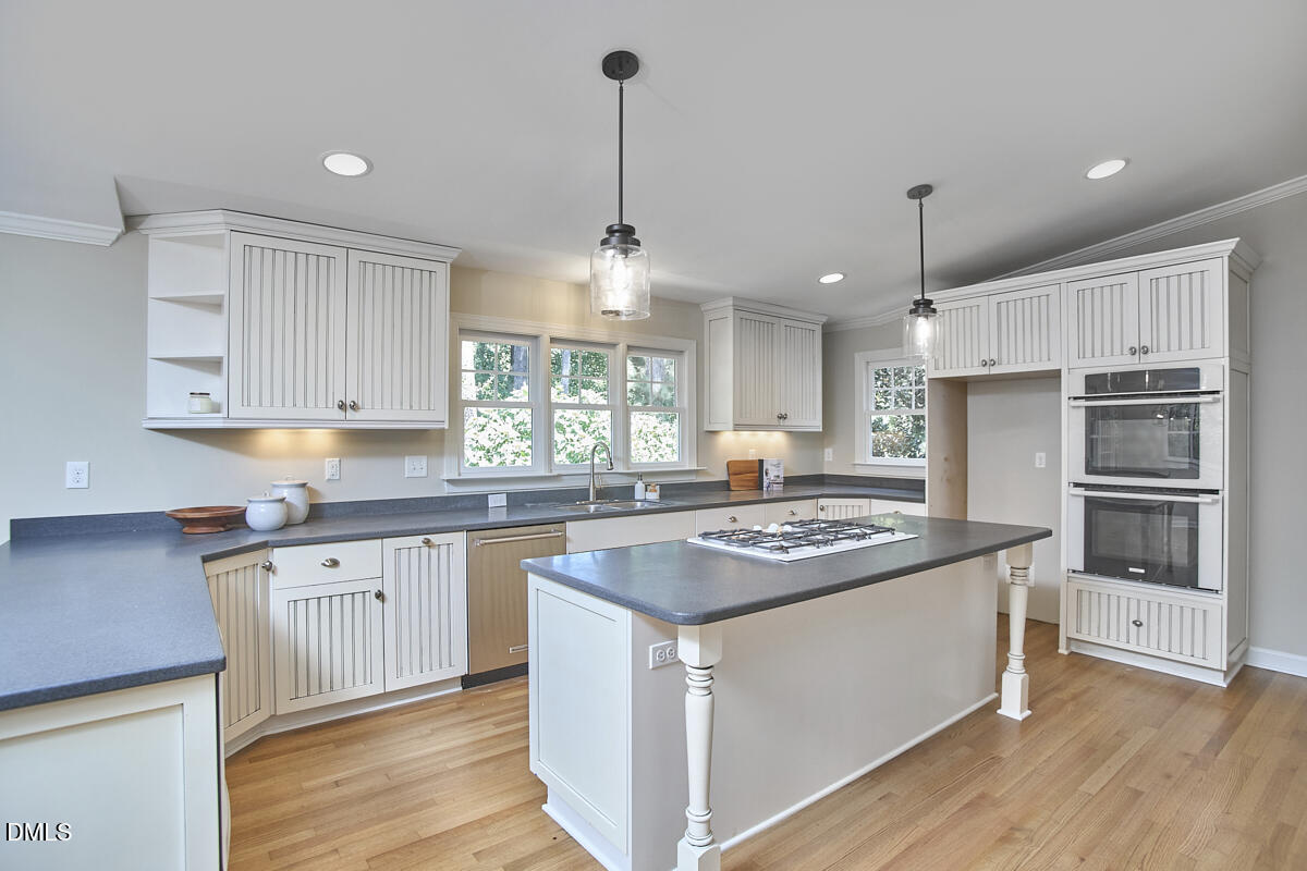 Kitchen with white paneled cabinets, a large cooktop island, double ovens, and hardwood floors.