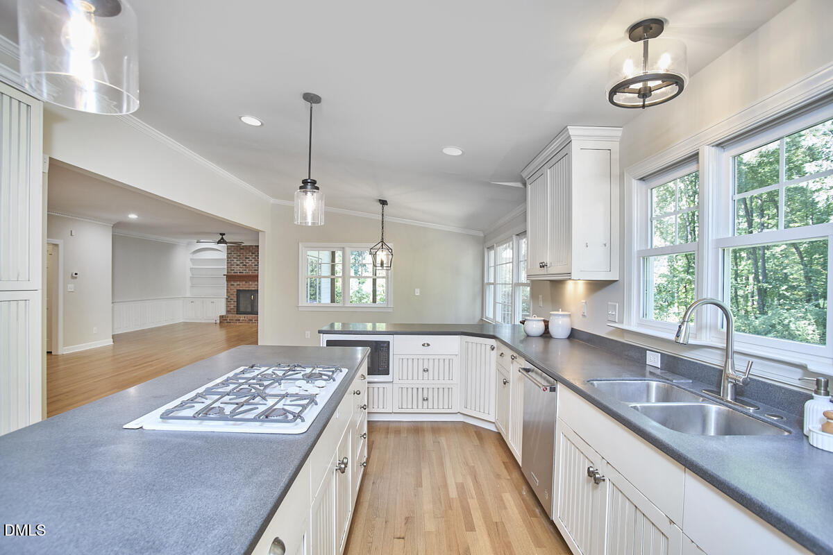 Vacant kitchen with a gas cooktop island, white cabinetry, gray counters, and windows overlooking trees.