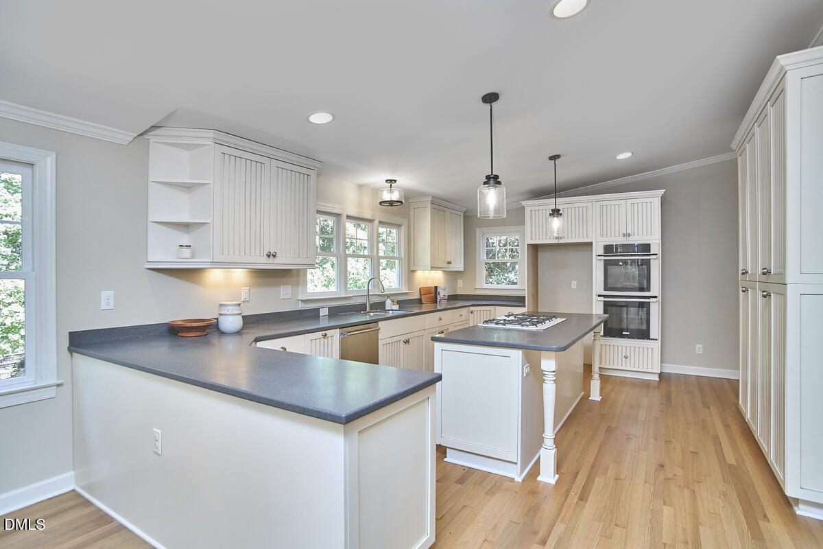 Kitchen with white cabinetry, dark counters, a central cooktop island, and double wall ovens.