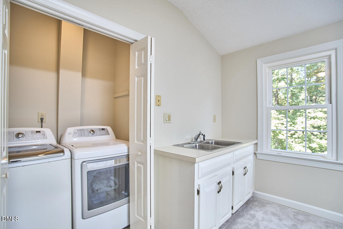 Laundry room with washer and dryer behind folding doors and a utility sink beside a large window.