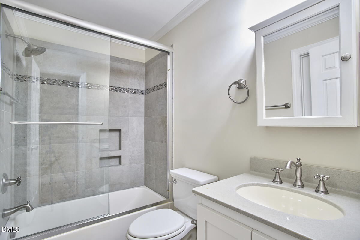 Bathroom with a glass-enclosed tub and shower, gray tile, and a white vanity with an oval sink.