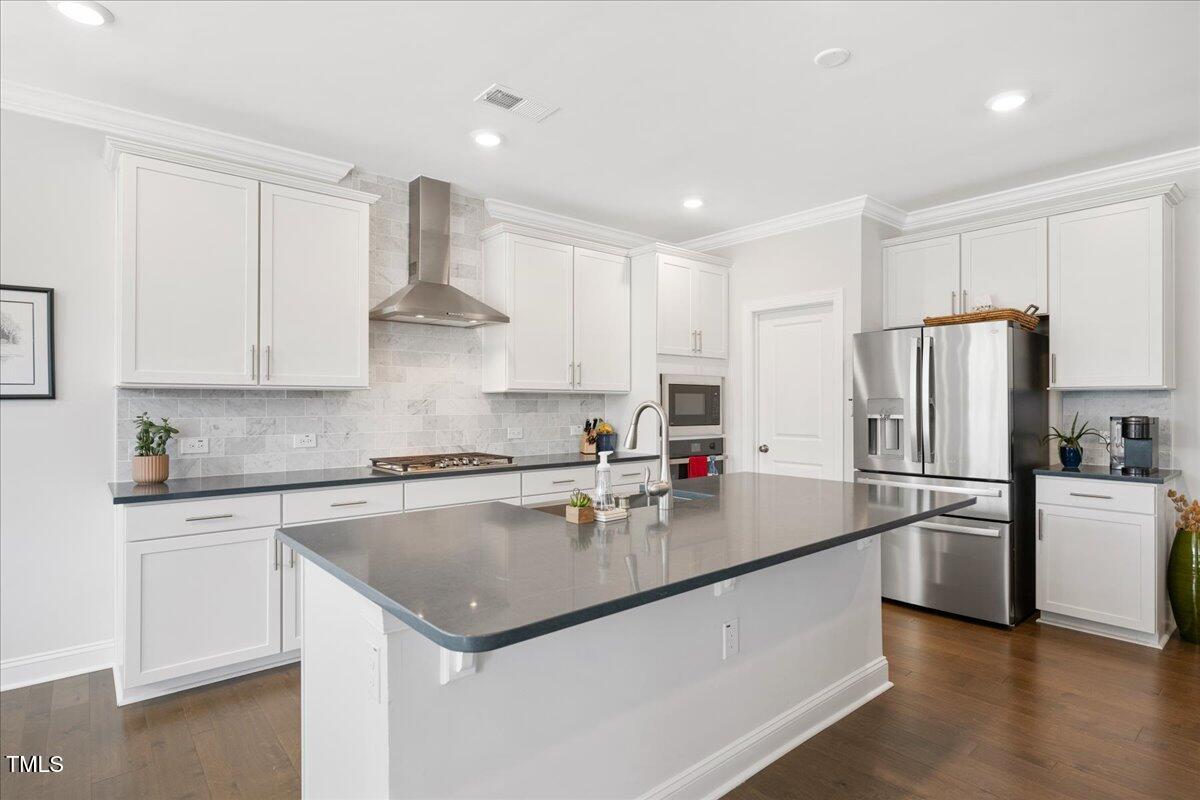 Modern kitchen with white cabinets, a large island, gray stone backsplash, and stainless steel appliances.