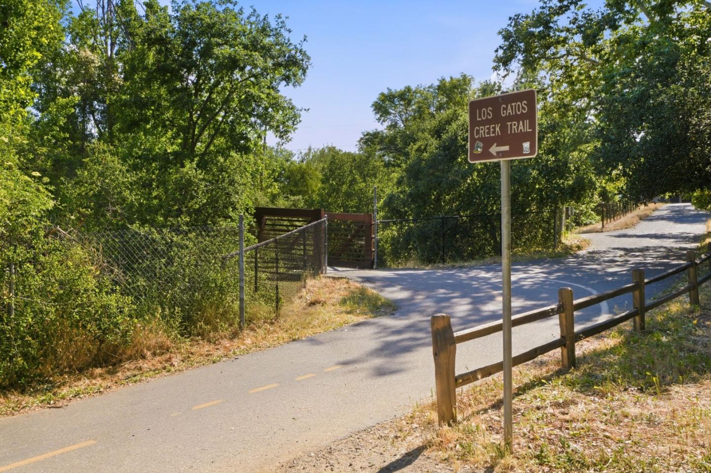 Paved Los Gatos Creek Trail entrance beneath trees, marked by a brown trail sign.