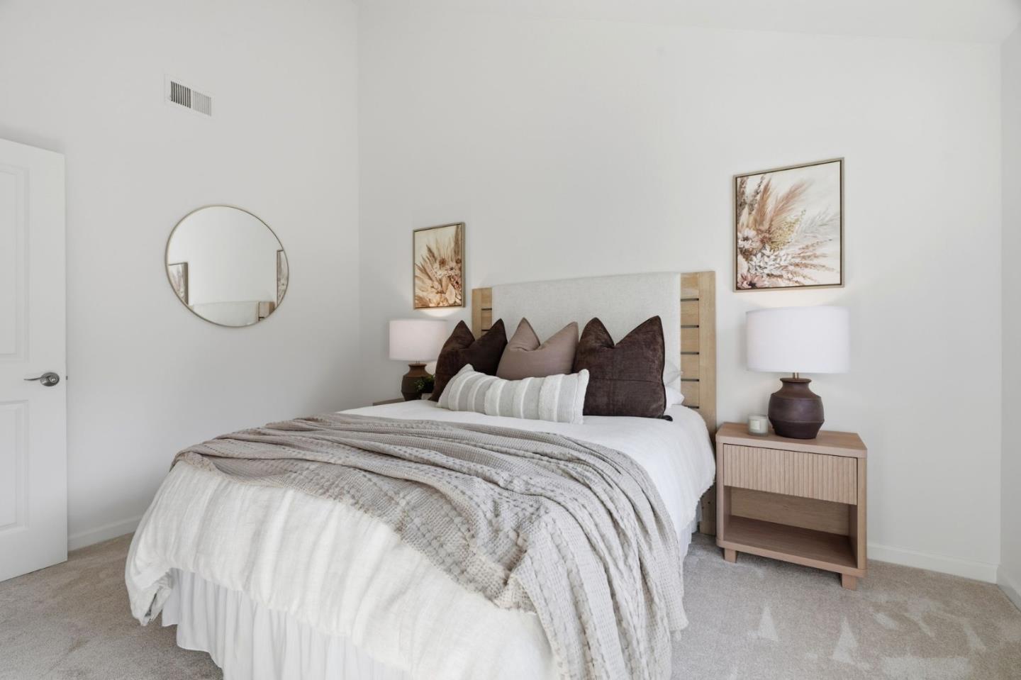 Staged bedroom with layered neutral bedding, a light wood headboard, and matching bedside decor.