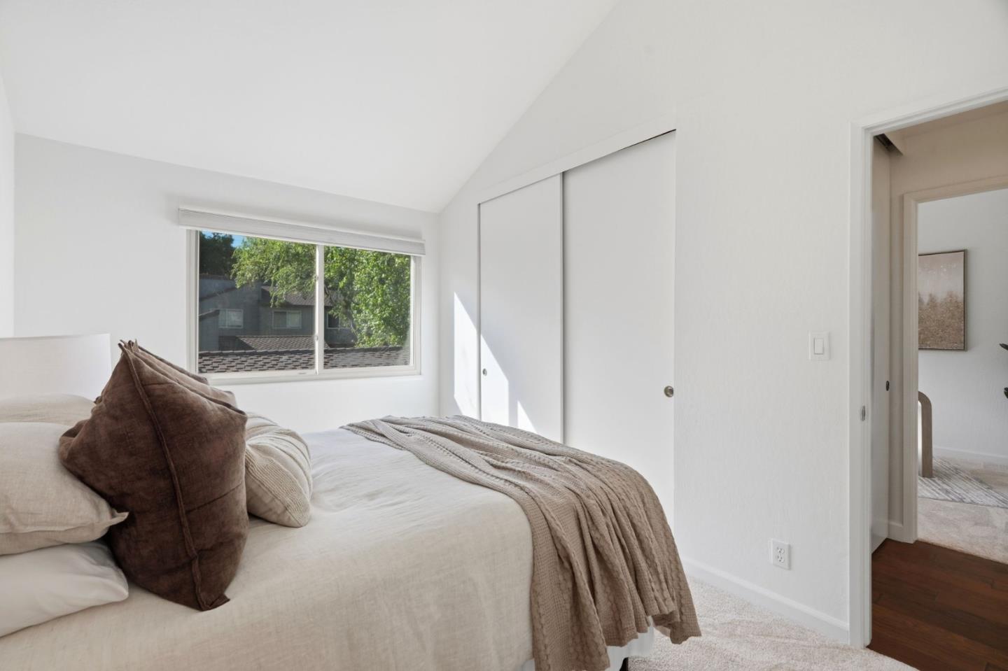 Bright staged bedroom with a large window, sliding closet doors, and neutral bedding.