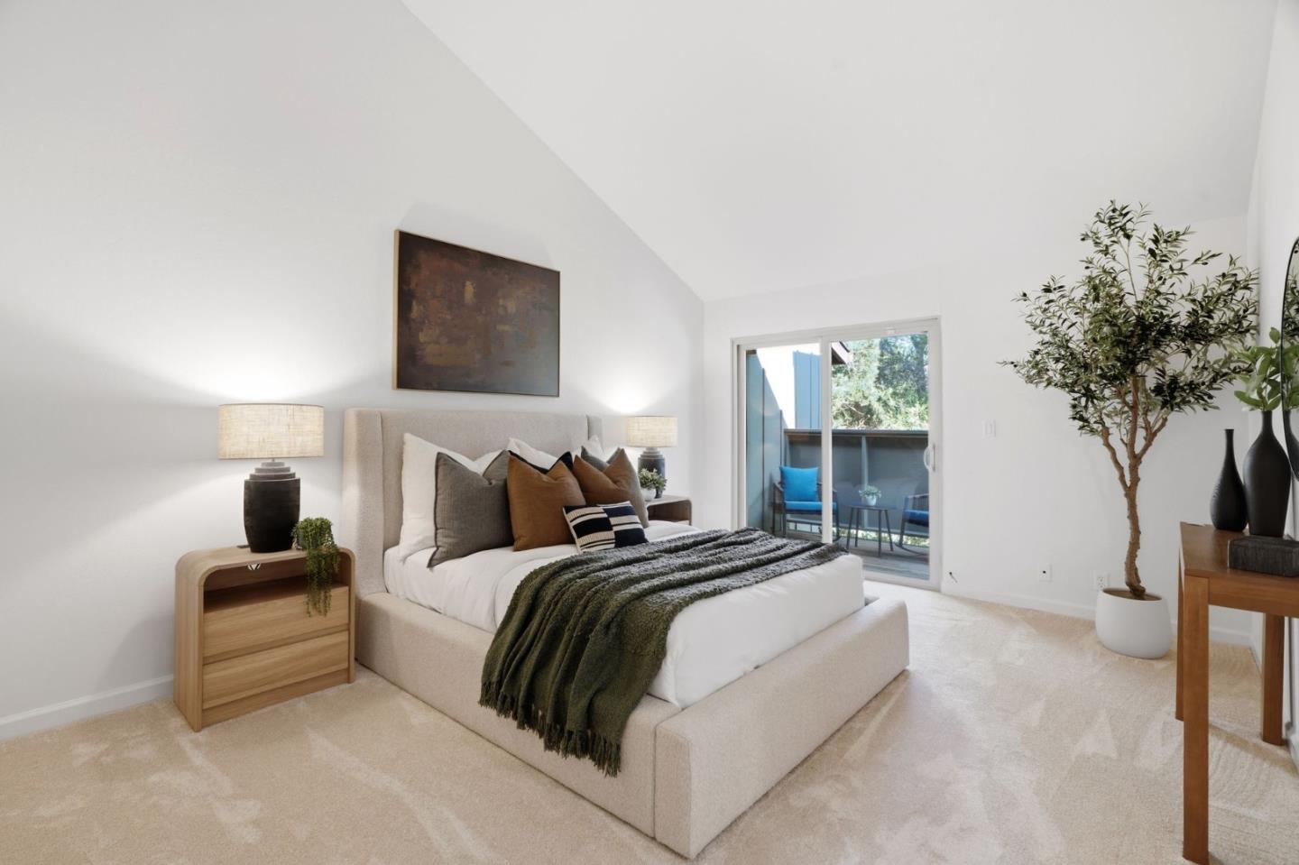 Staged bedroom with a cream bed, vaulted ceiling, and sliding glass door to a balcony.