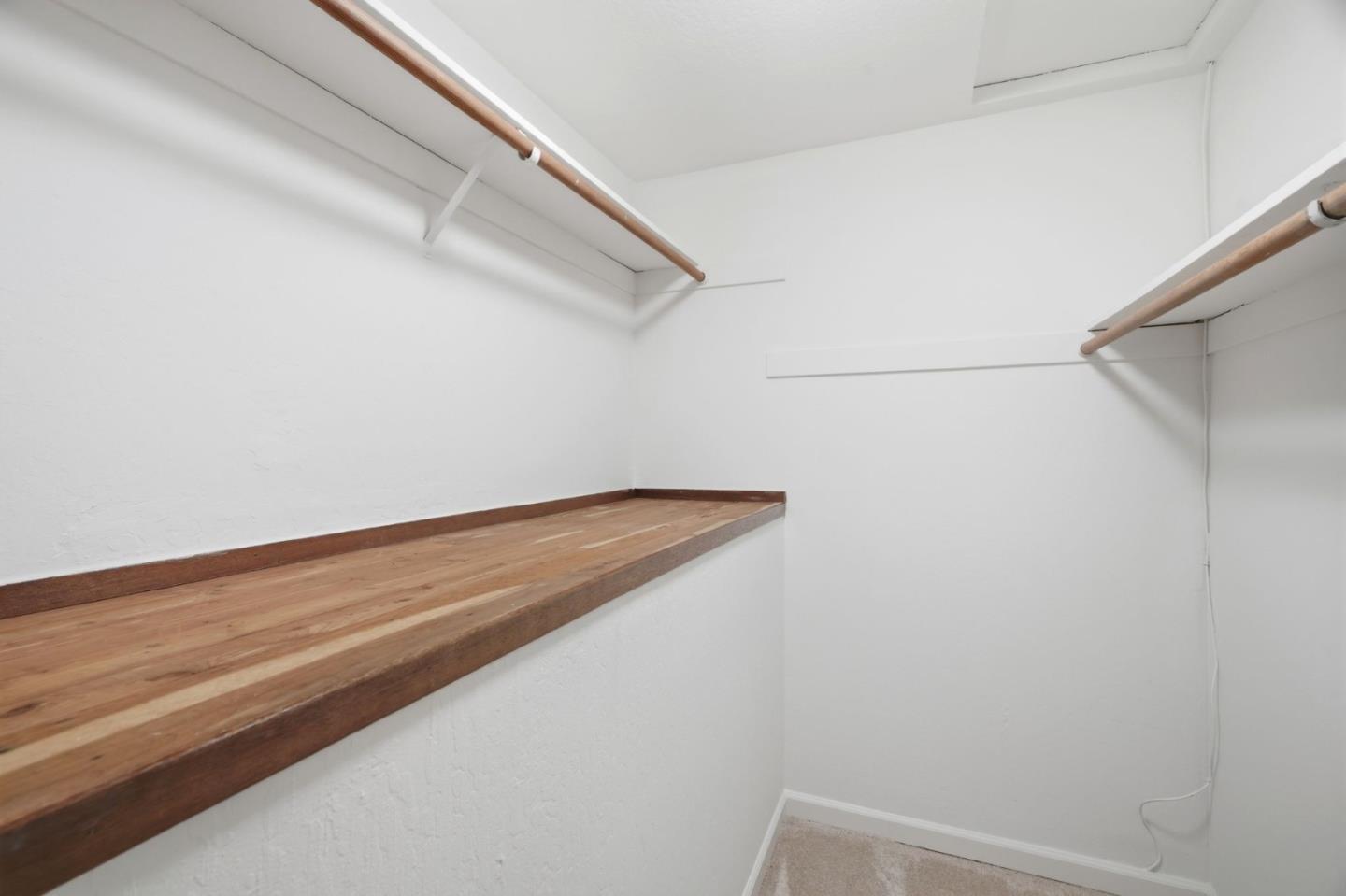 Walk-in closet with wooden shelving and overhead hanging rods.