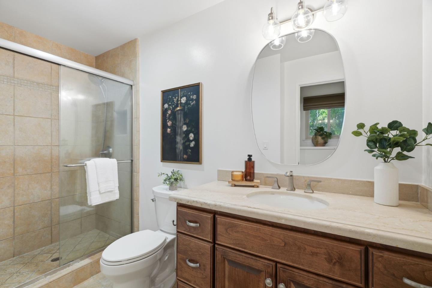 Bathroom with a glass-enclosed tile shower and dark wood vanity beneath an oval mirror.