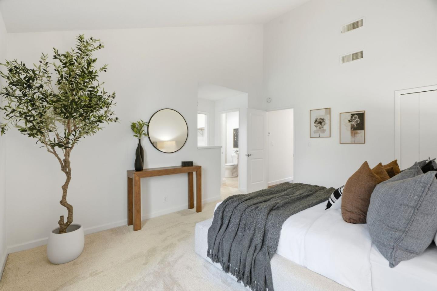 Bright staged bedroom with a vaulted ceiling, gray throw, and doorway to a bathroom.