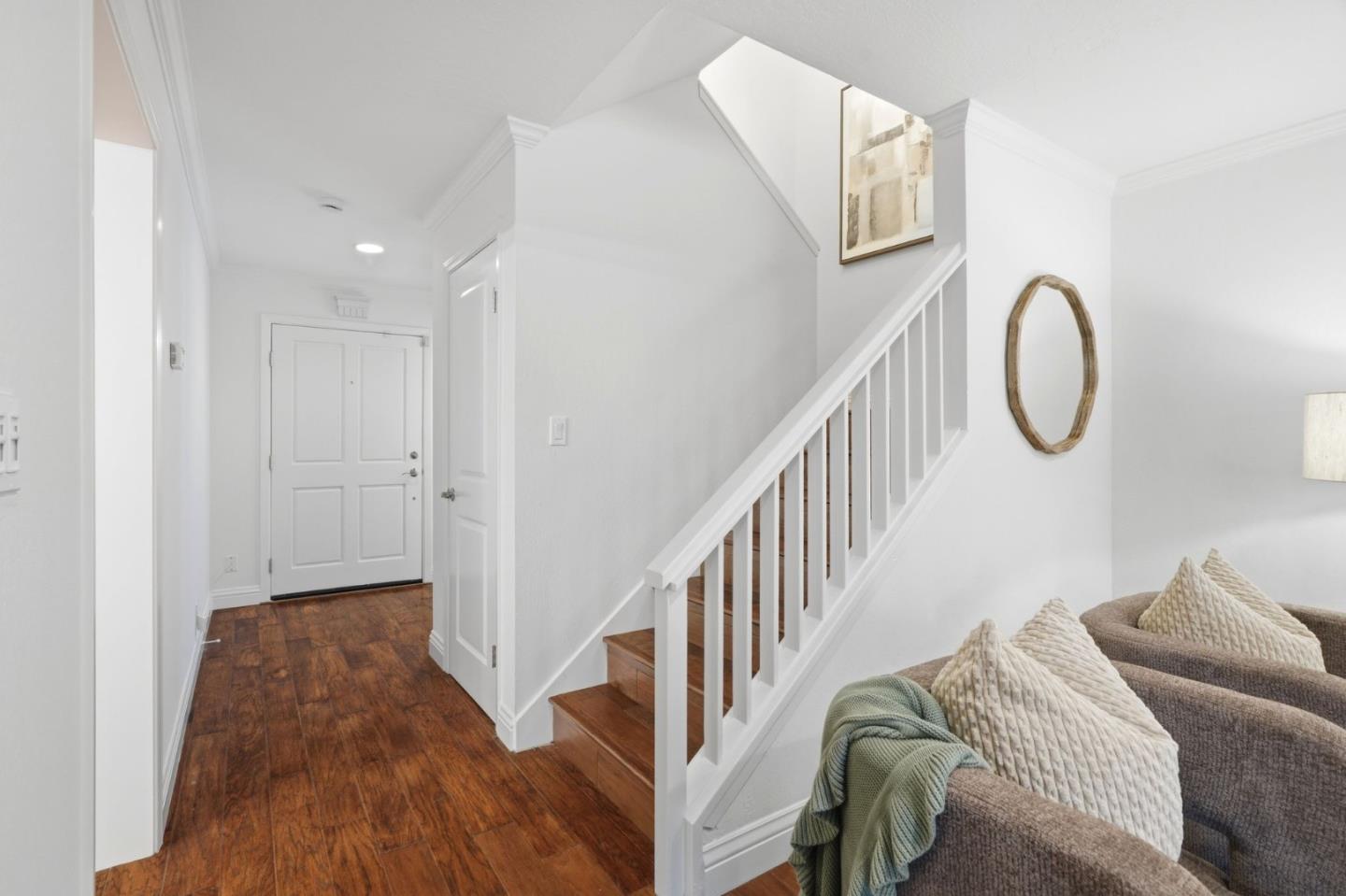 Entryway with dark wood flooring, white front door, and staircase beside a sofa.
