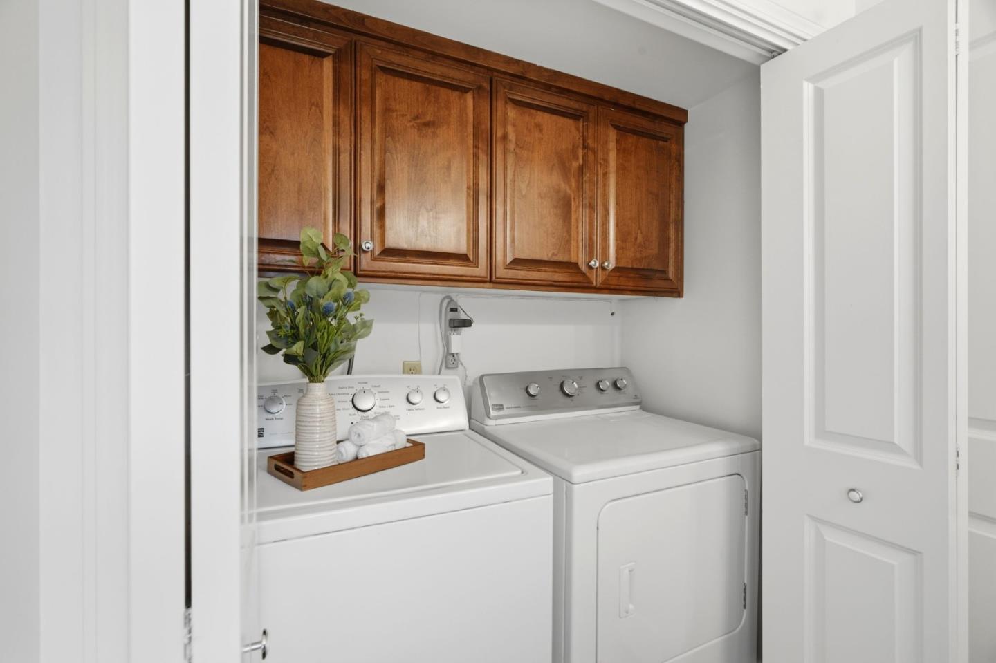 Laundry room with white washer and dryer beneath wood cabinets.