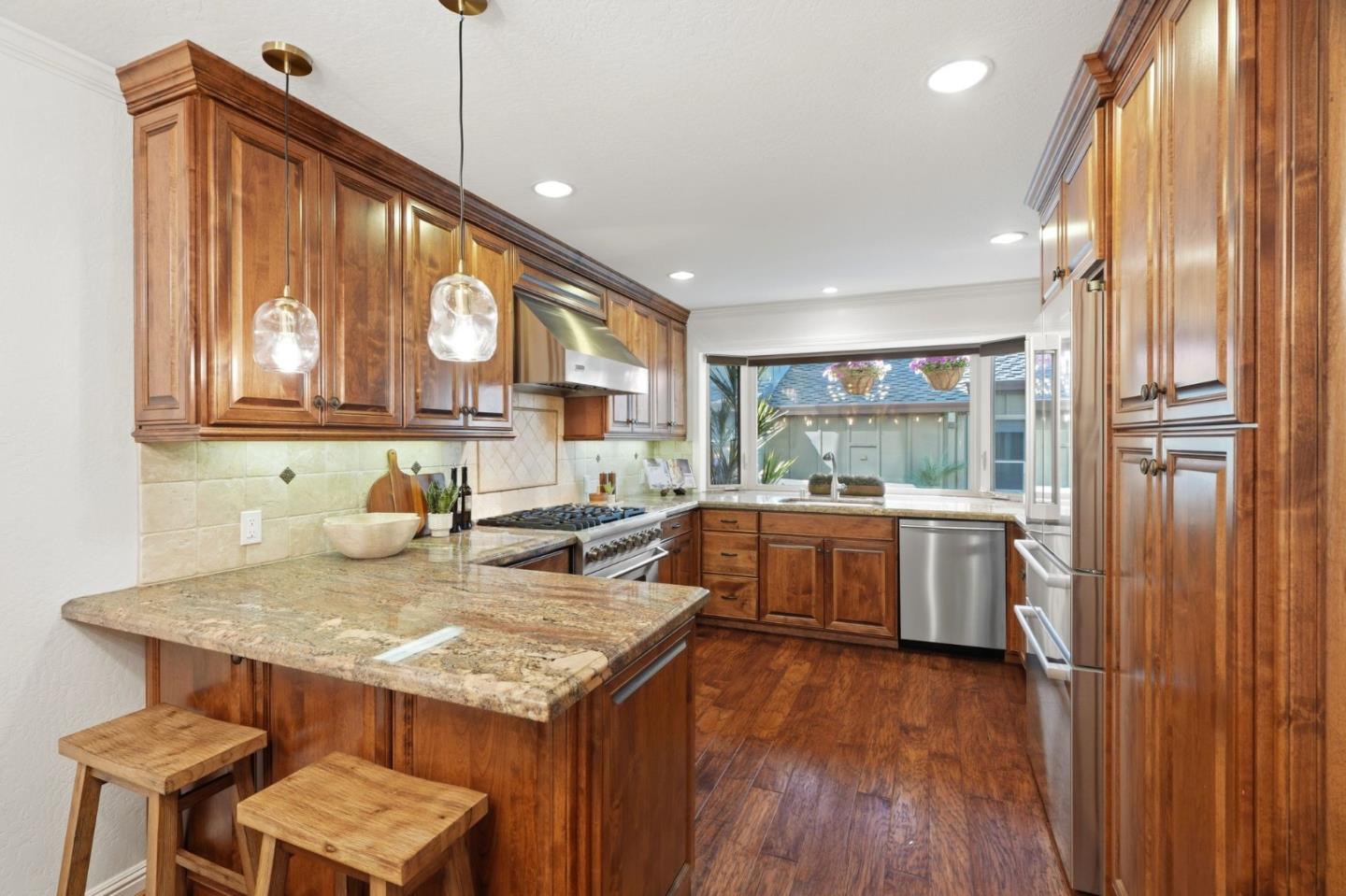Kitchen with rich wood cabinets, granite counters, stainless steel appliances, and a wide window above the sink.