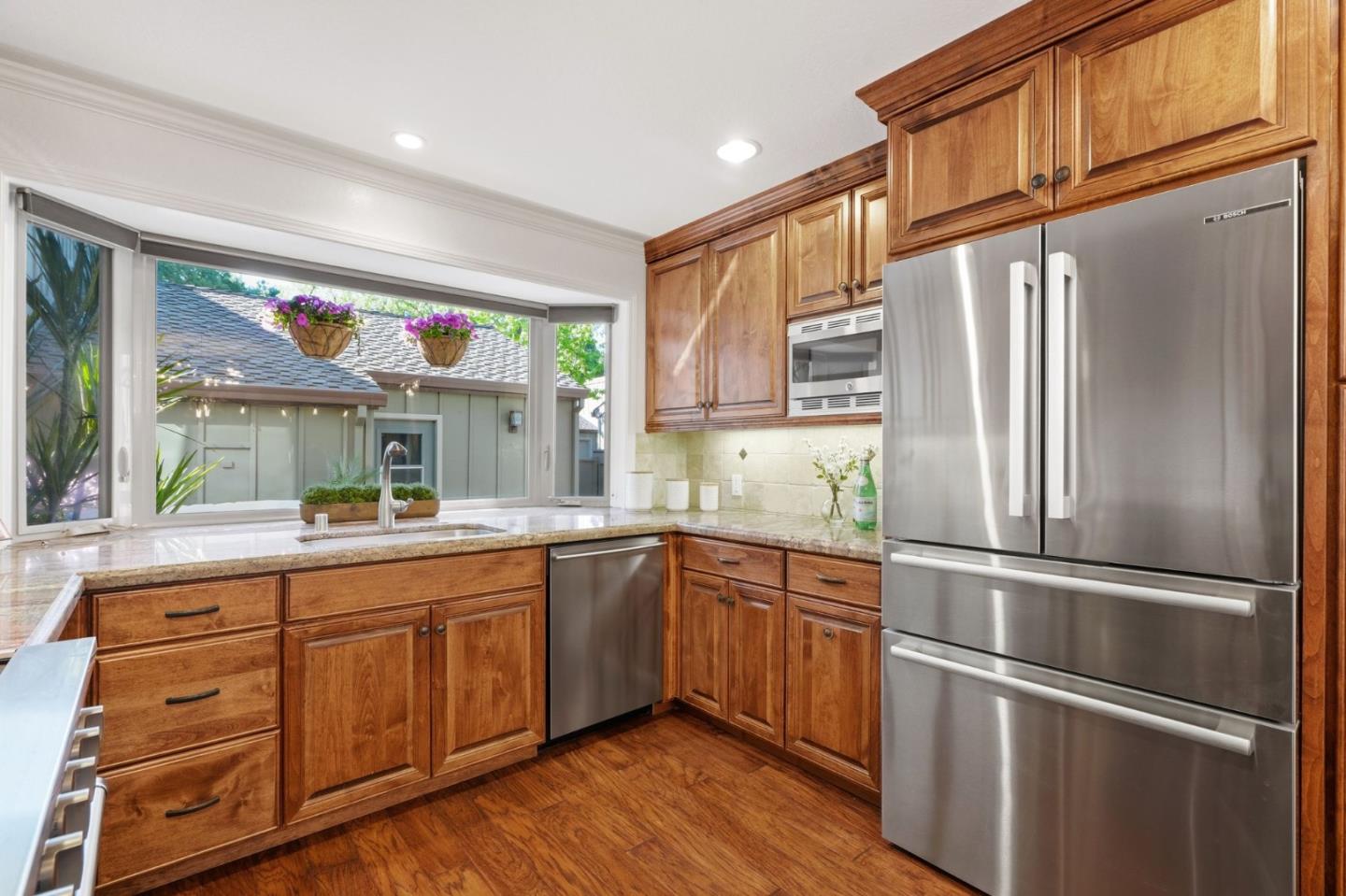 Kitchen with wood cabinets, stainless steel appliances, and a wide sink window with hanging flower baskets.
