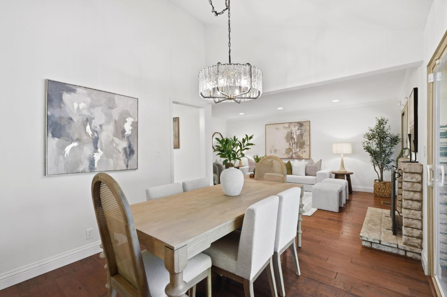 Open-plan dining and living room with a wood table, crystal chandelier, and stone fireplace.