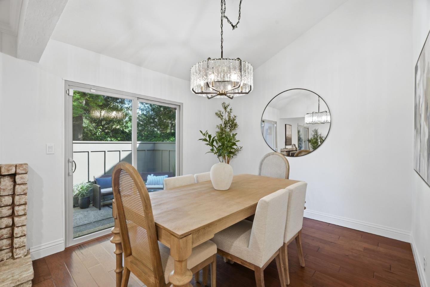 Furnished dining room with a wooden table, crystal chandelier, and sliding doors to a leafy patio.