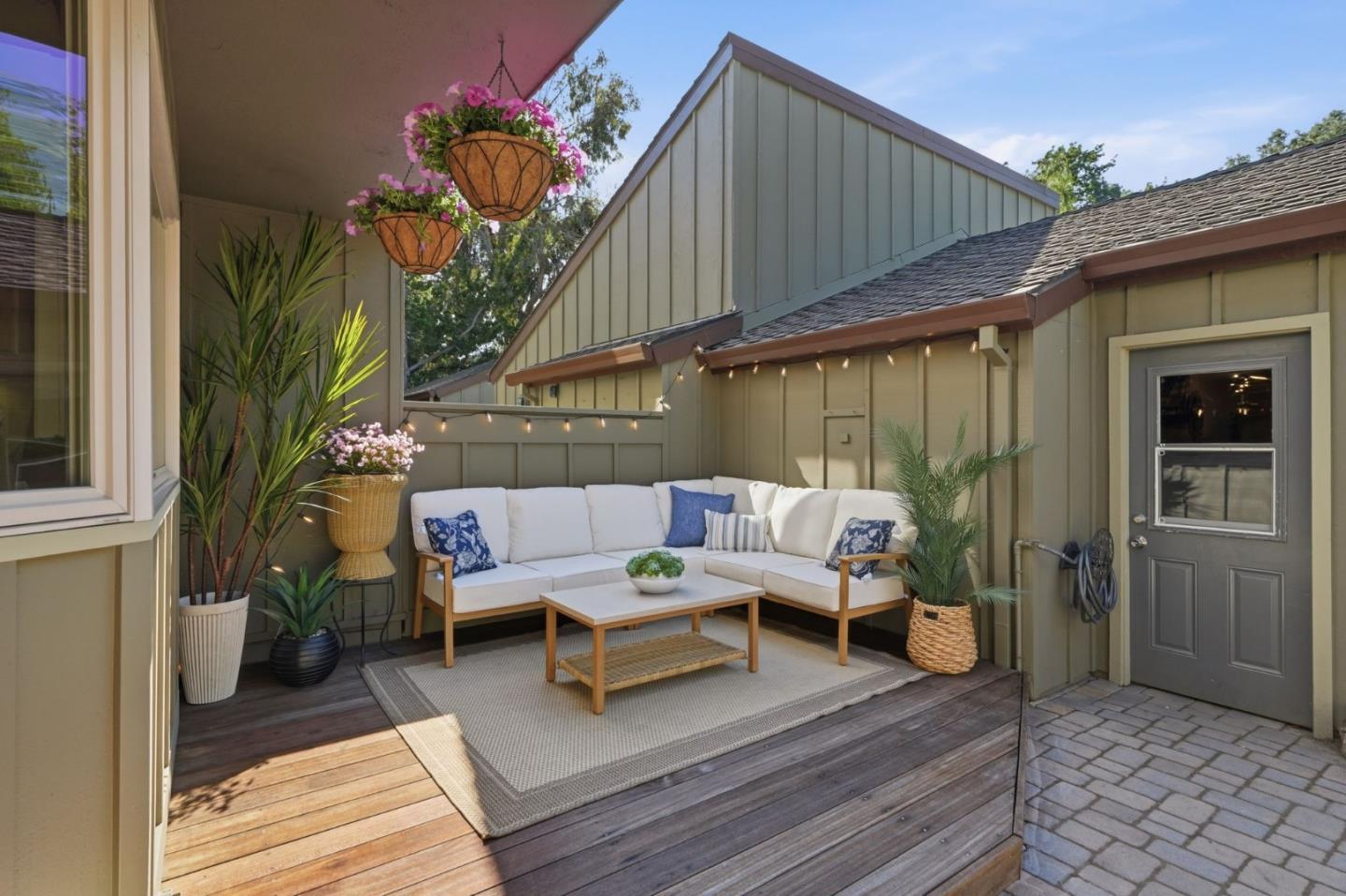 Covered patio with white sectional seating, potted plants, and string lights.