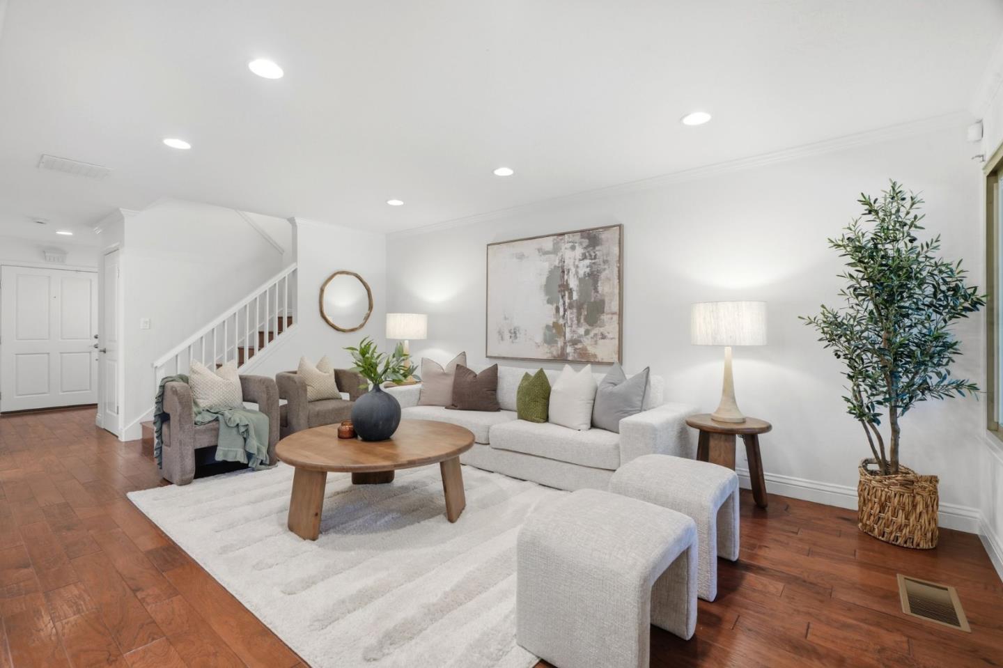 Staged living room with a white sofa, wood coffee table, hardwood floors, and staircase.
