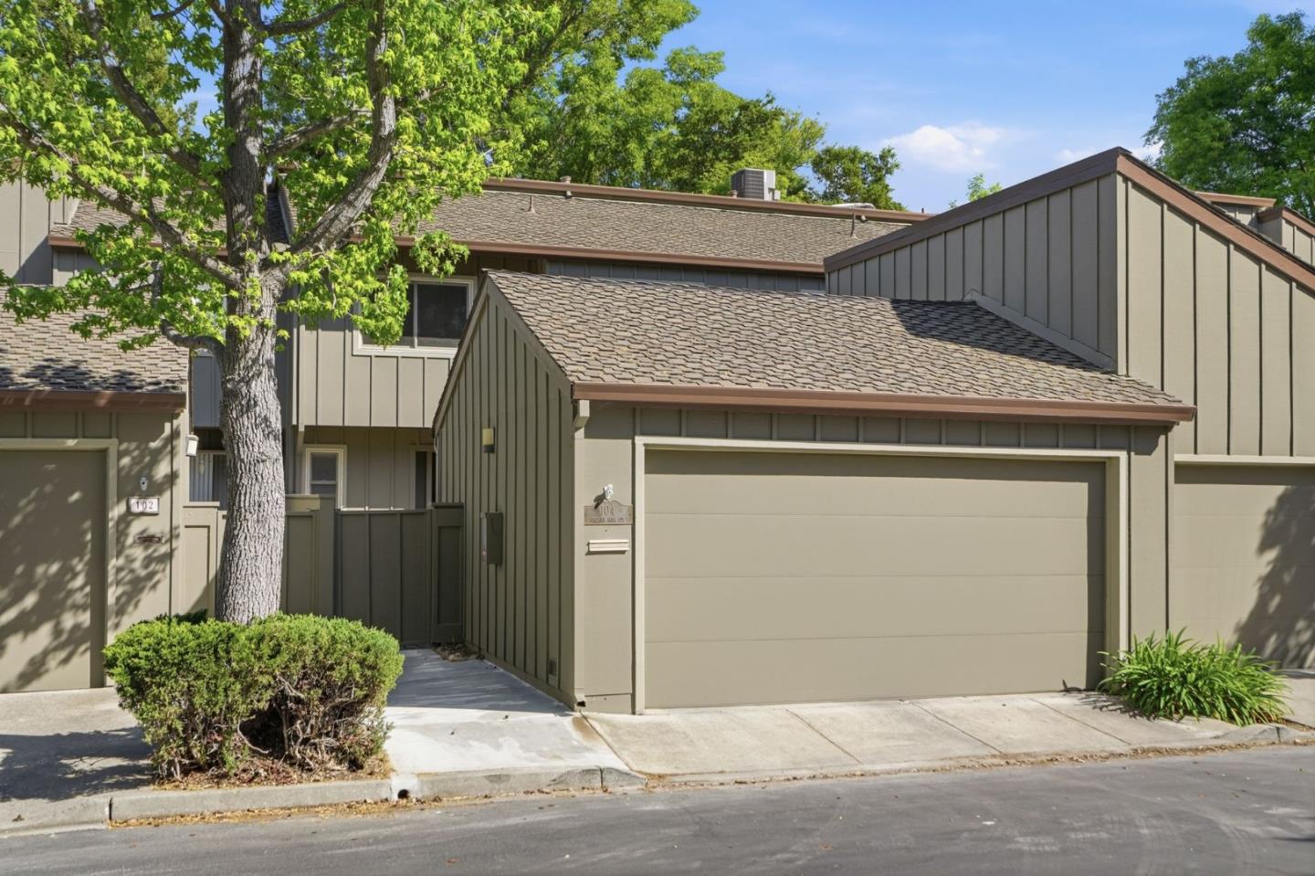 Townhouse exterior with a large garage, shaded entry, and mature trees.
