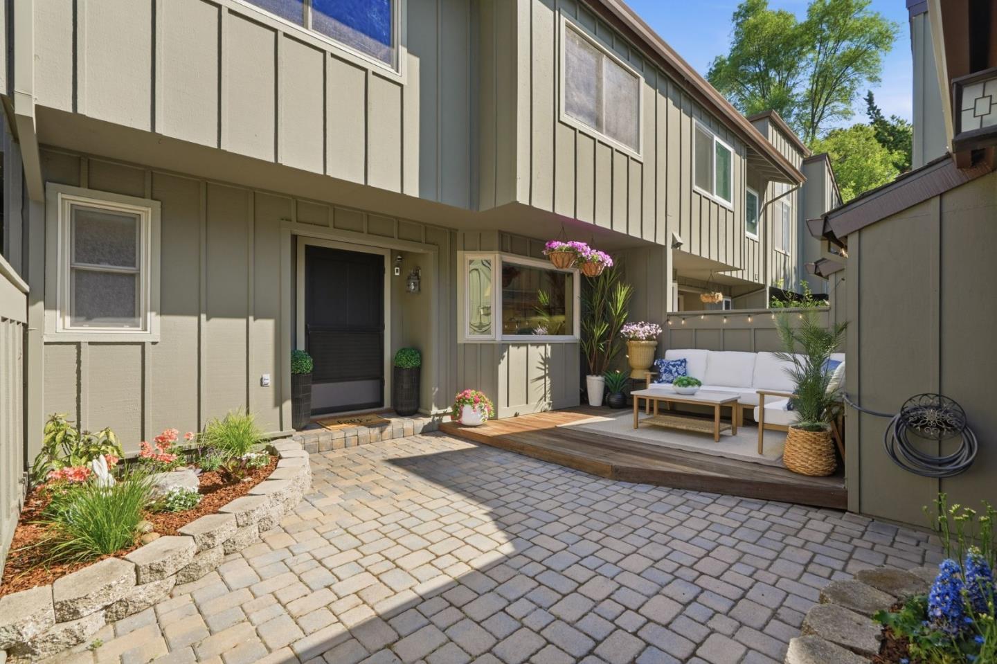 Home courtyard with a paved entry, raised deck, outdoor sofa, and flowering plants.