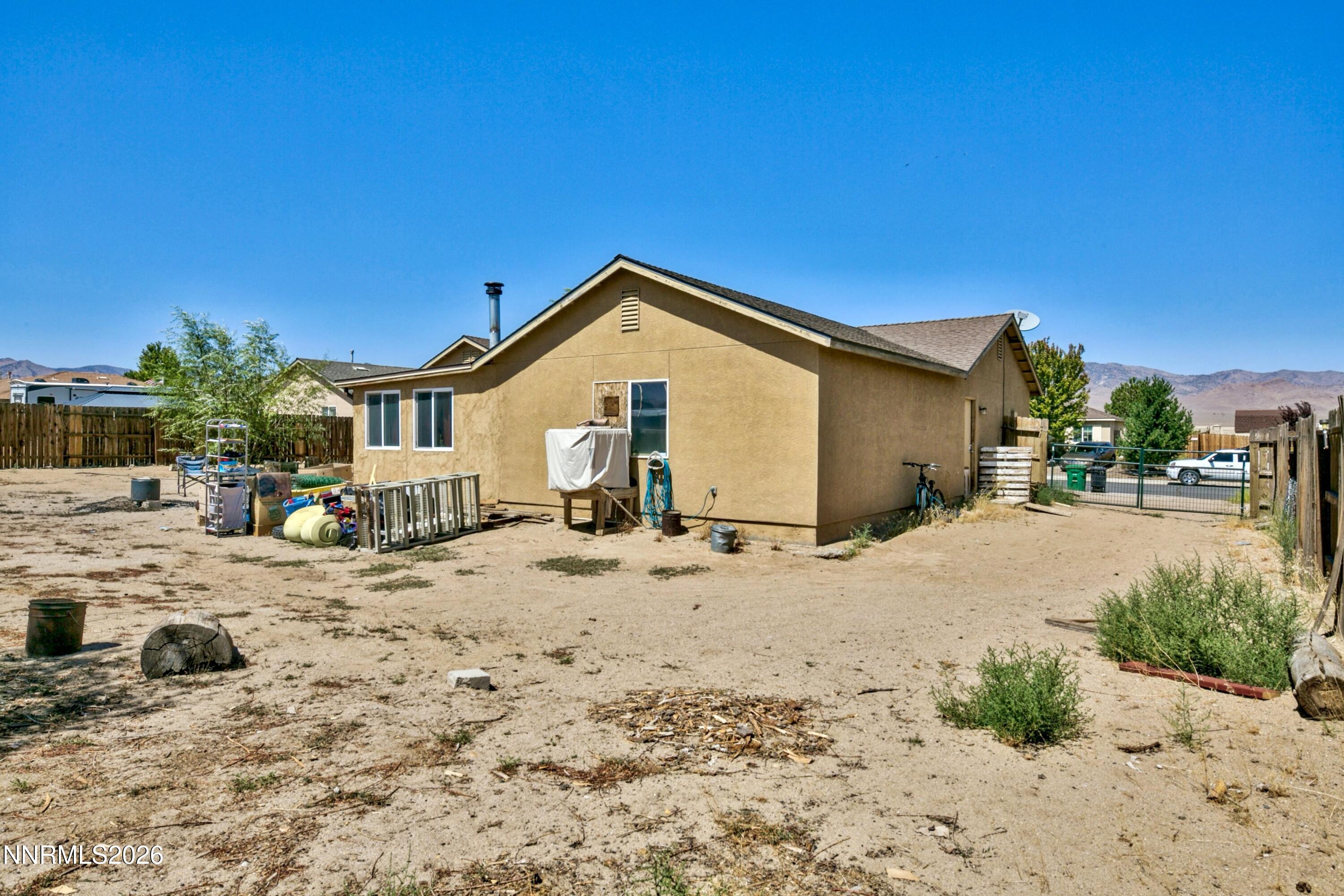 Rear of a tan single-story house with a large sandy yard and distant mountains.
