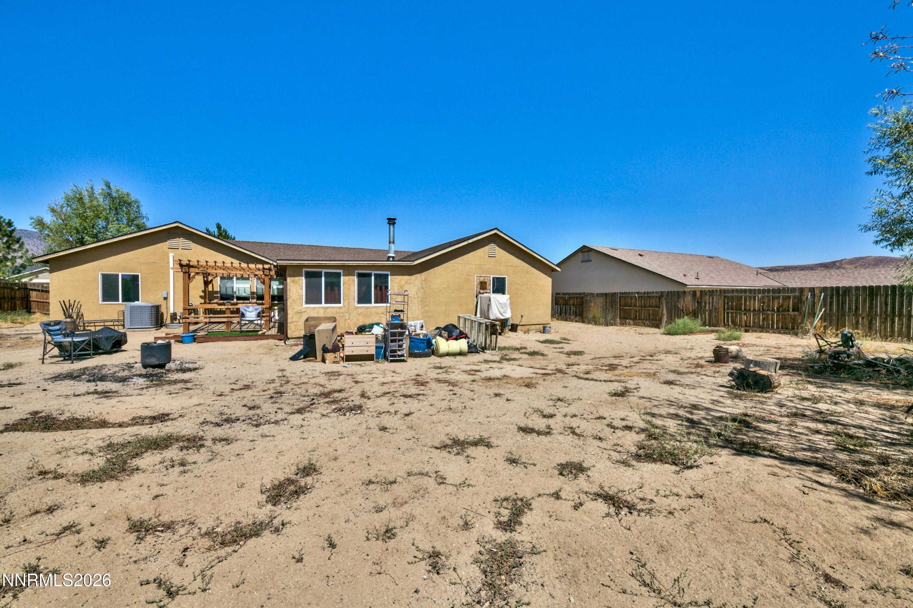 Tan stucco home with a wooden pergola and a wide, mostly bare fenced backyard.