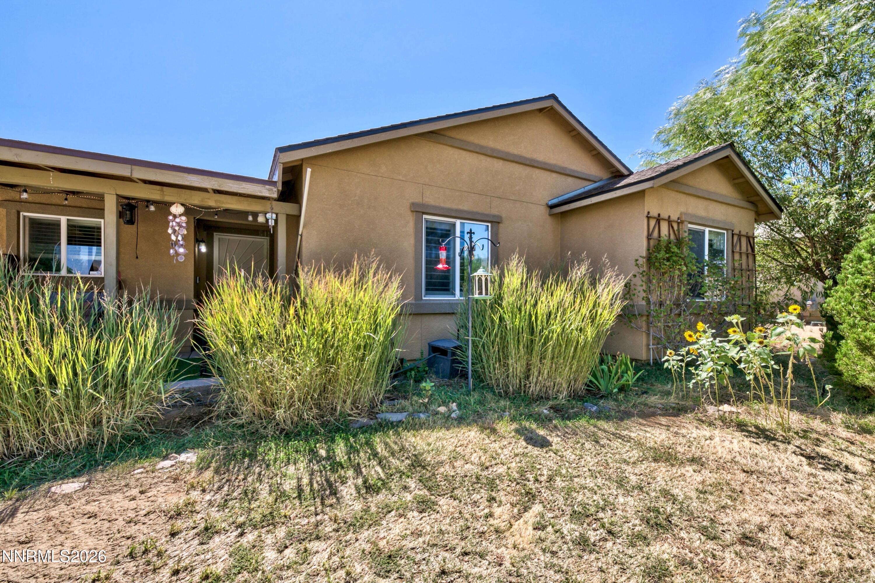Tan single-story home with a covered patio, tall ornamental grasses, and a sunny garden.
