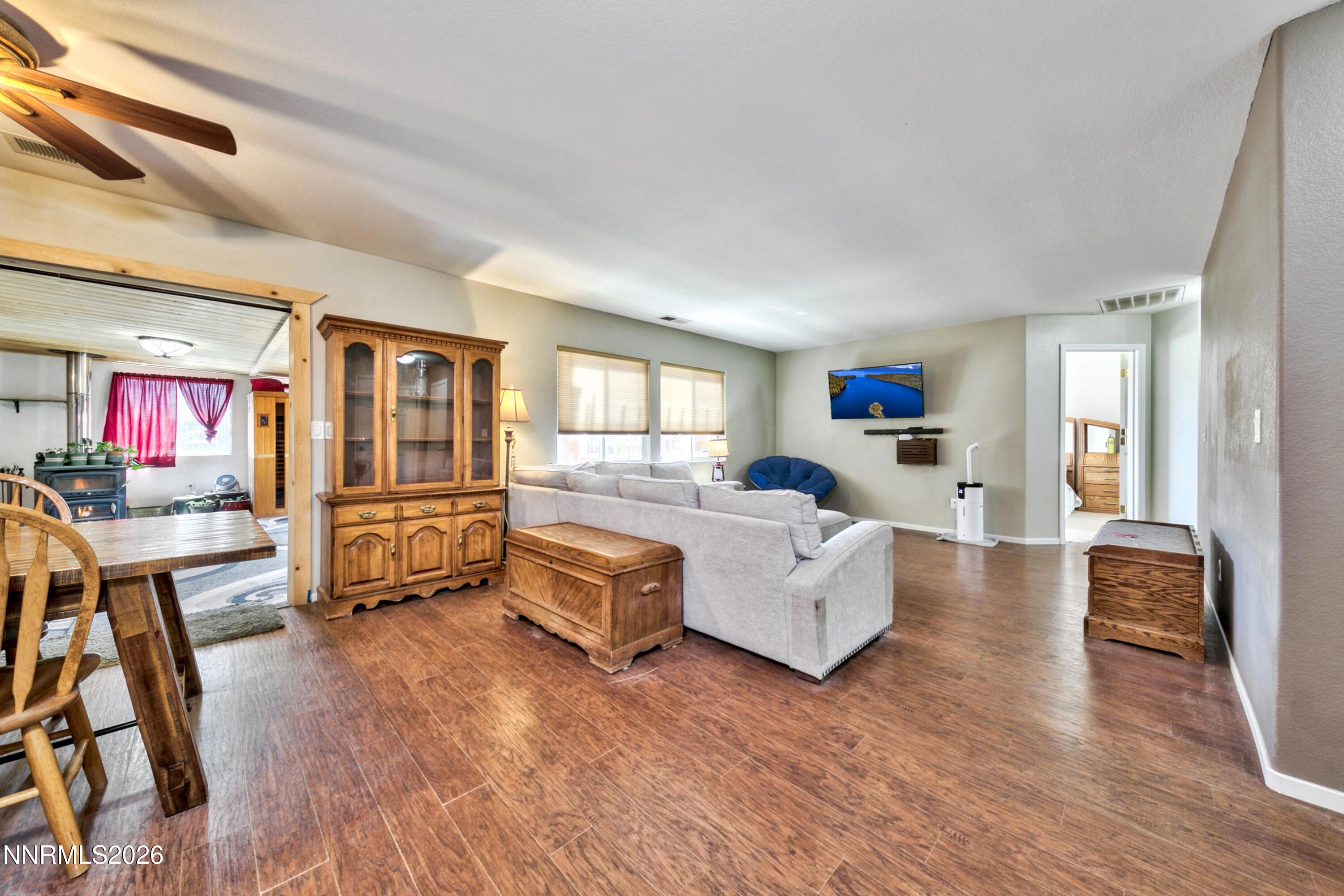 Living and dining area with a gray sectional, wood-look floors, and an adjoining room with a wood stove.