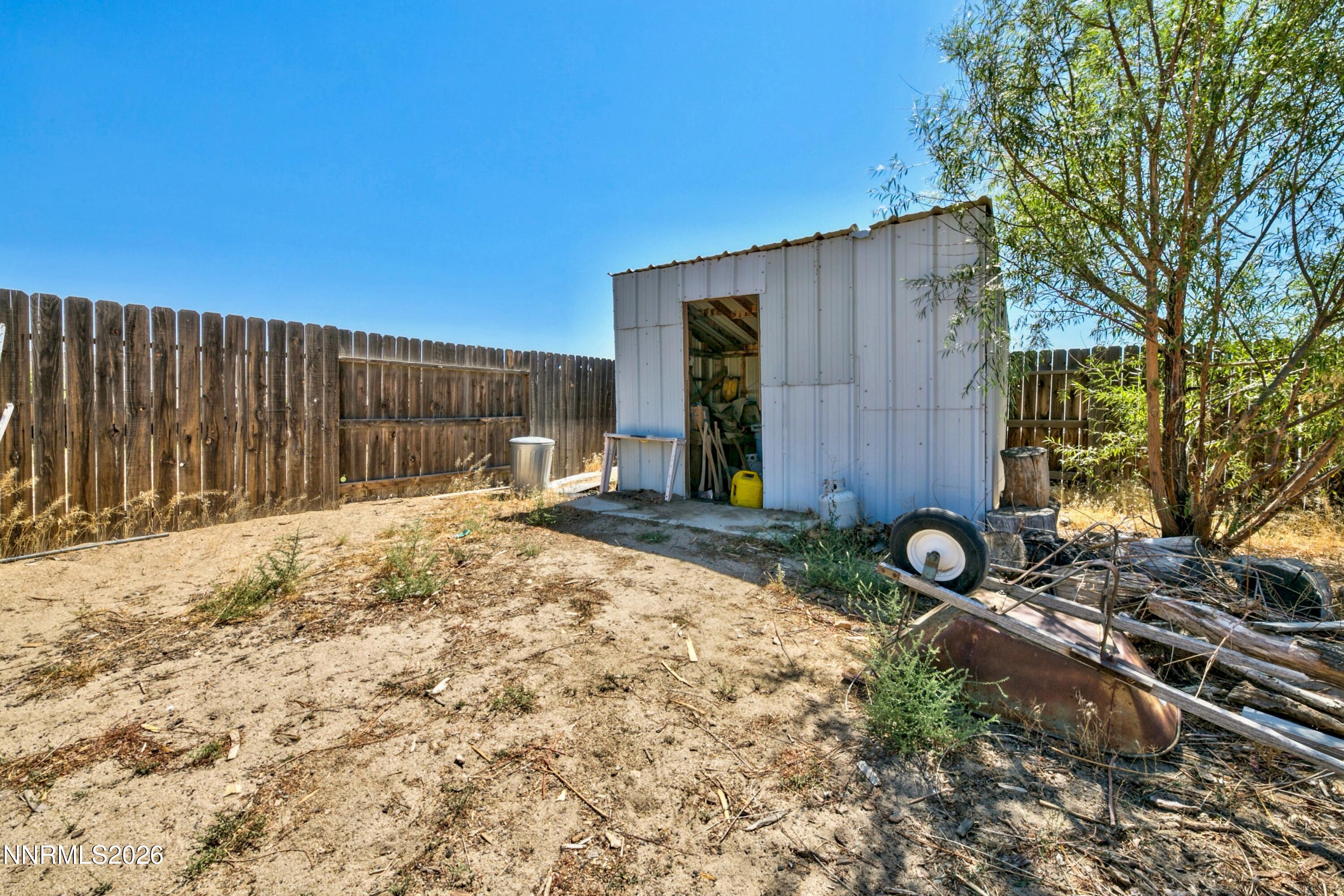 Dry fenced backyard with a white metal storage shed and scattered yard equipment.