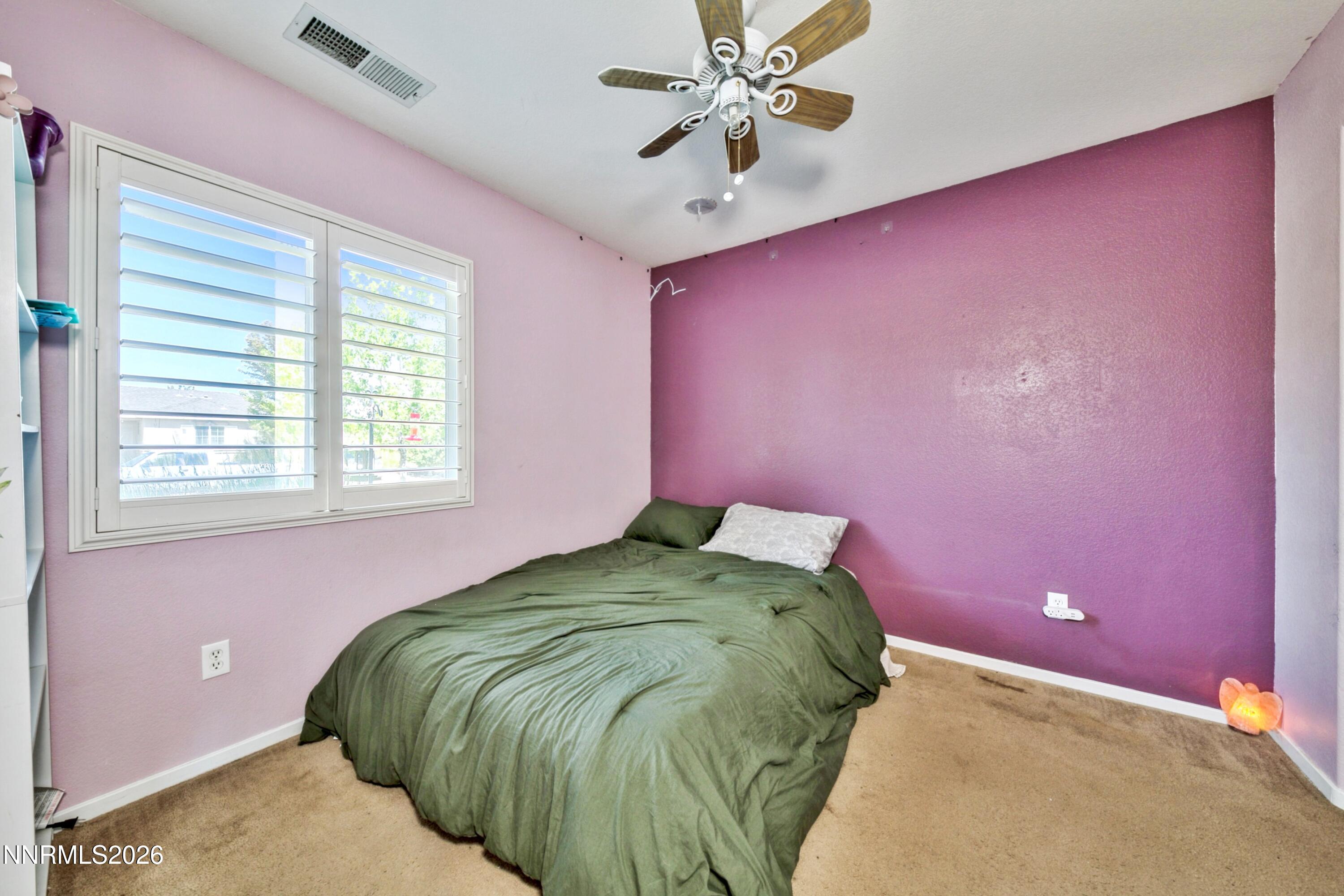 Bedroom with green bedding, magenta accent wall, and plantation-shuttered windows.