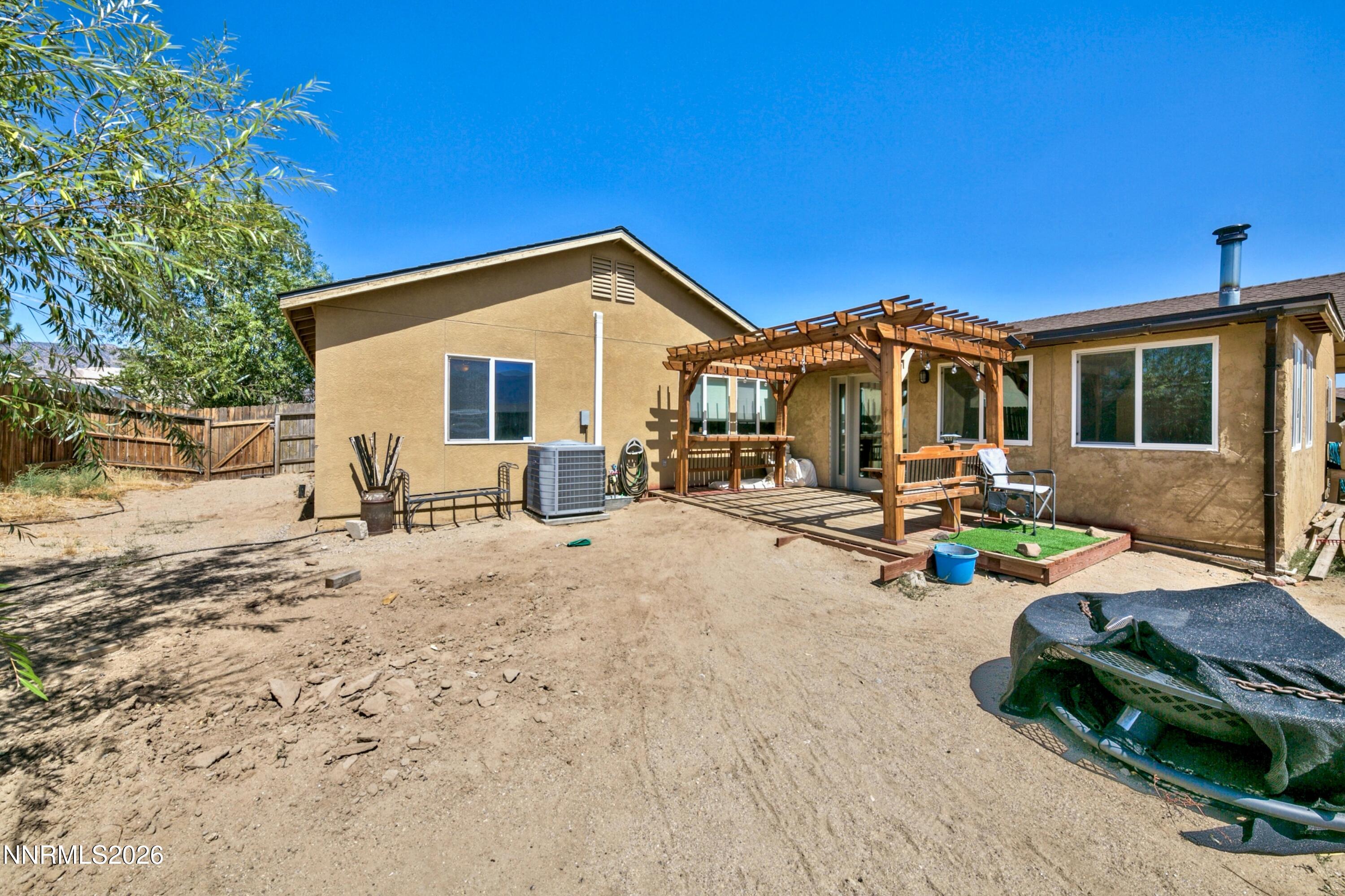 Rear of tan stucco home with a wooden pergola over the patio and a dry fenced yard.