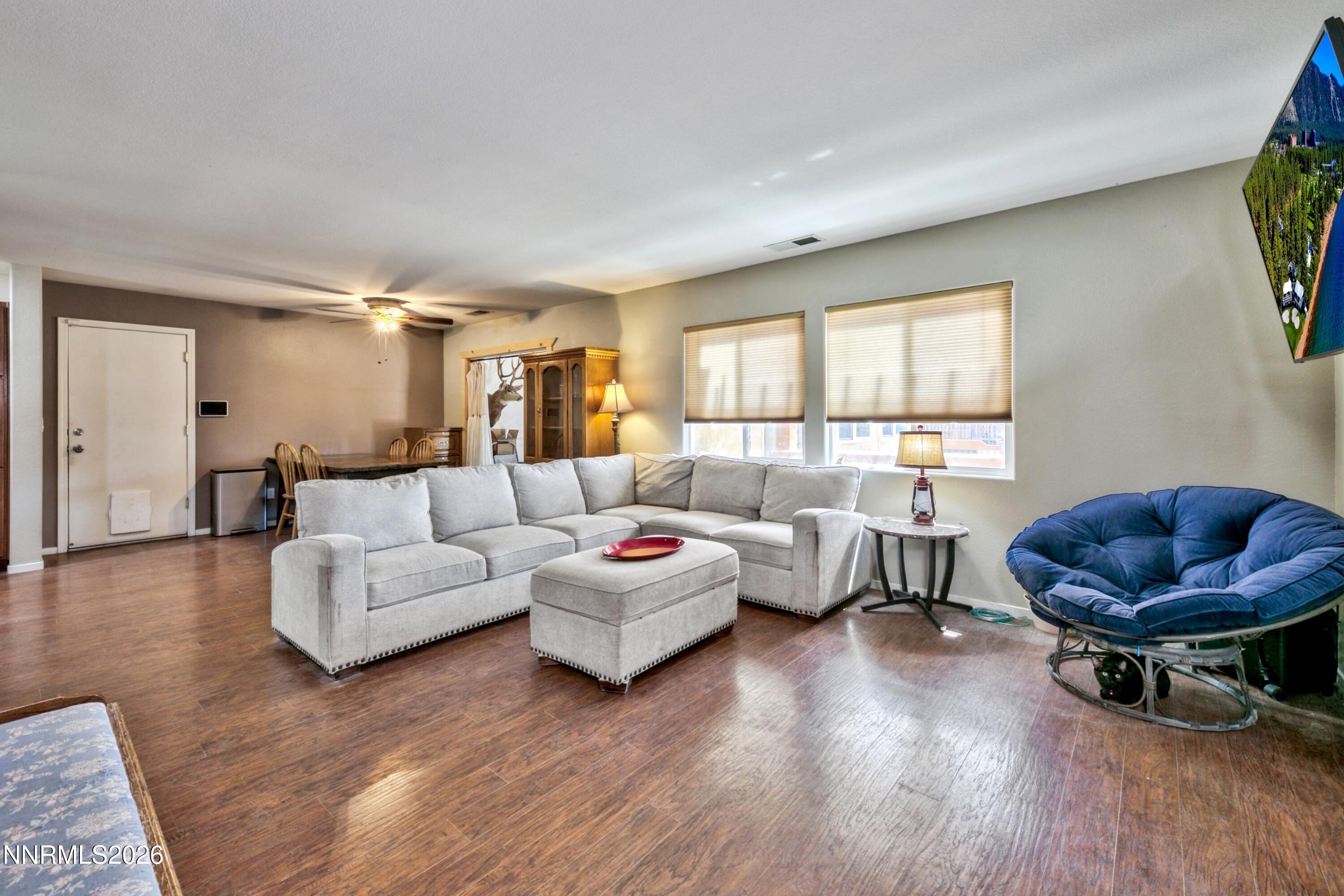 Living room with a light-gray sectional, matching ottoman, and blue papasan chair on dark wood-look flooring.