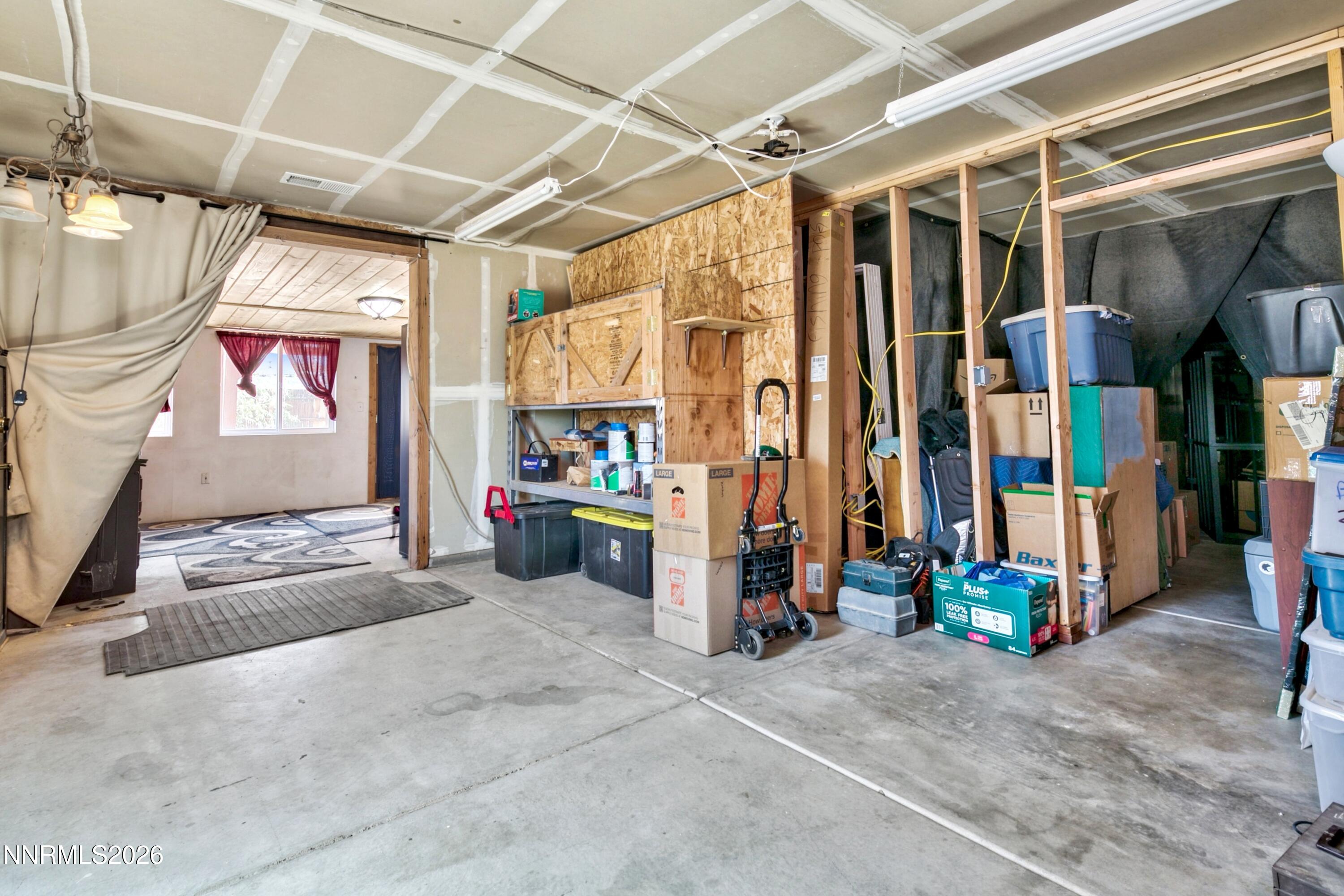 Garage with exposed framing and ceiling, storage boxes and bins, and an open doorway to a room.